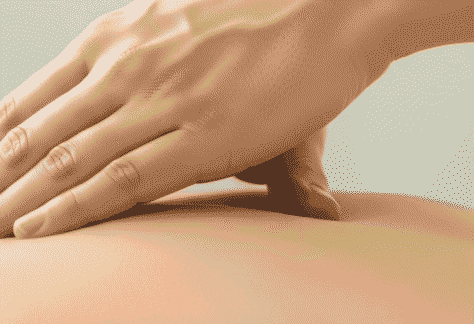 Eine Nahaufnahme einer professionellen Hand, die sanft den oberen Rücken massiert, mit warmem Licht, das die Haut und die Berührung betont, symbolisierend tiefe Entspannung und heilsame Tantra Massage.