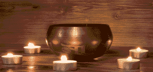 Ein traditioneller Gong, umgeben von mehreren brennenden Teelichtern, auf einem rustikalen Holzuntergrund, symbolisierend Klangheilung, Meditation und die tiefe Resonanz in der Tantra Massage und spirituellen Praxis.