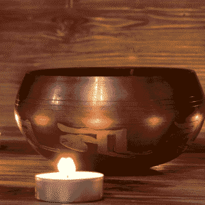 Ein traditioneller Gong, umgeben von mehreren brennenden Teelichtern, auf einem rustikalen Holzuntergrund, symbolisierend Klangheilung, Meditation und die tiefe Resonanz in der Tantra Massage und spirituellen Praxis.