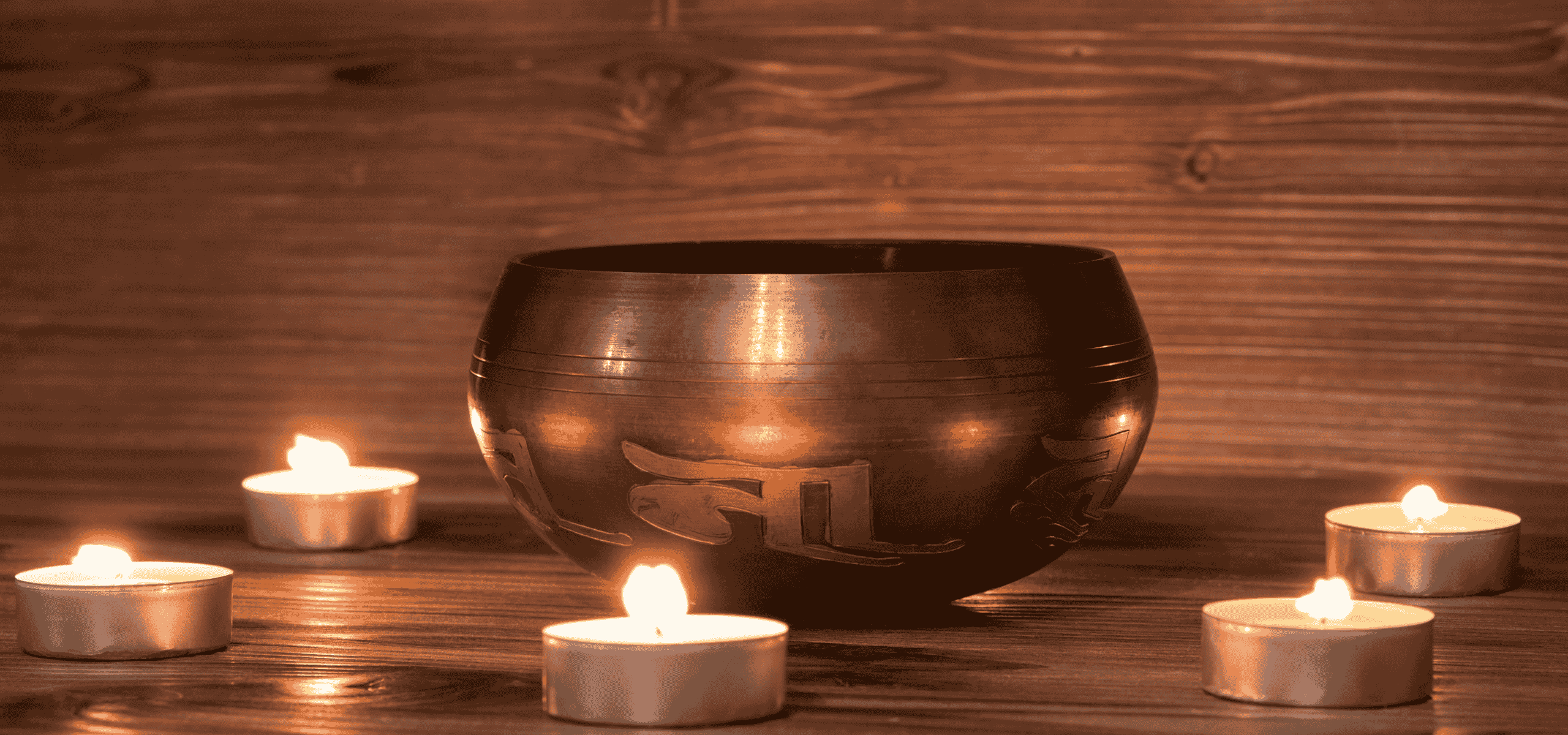 Ein traditioneller Gong, umgeben von mehreren brennenden Teelichtern, auf einem rustikalen Holzuntergrund, symbolisierend Klangheilung, Meditation und die tiefe Resonanz in der Tantra Massage und spirituellen Praxis.