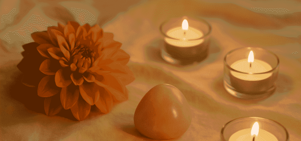 Warme Atmosphäre mit orangefarbener Blüte, spirituellem Stein und Kerzenlicht. Symbolisiert achtsame Berührung und Tantra Massage lernen.